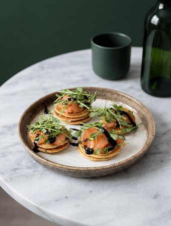 Lėkštėje patiekti užkandžiai su rūkyta lašiša, mikrožalumynais ir balzamiko padažu ant marmurinio stalo.